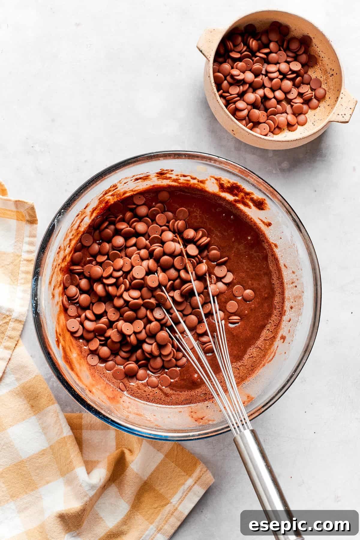 Folding chocolate chips into the prepared chocolate muffin batter. Generous amount of chocolate chips are gently folded into the chocolate muffin batter in a mixing bowl.