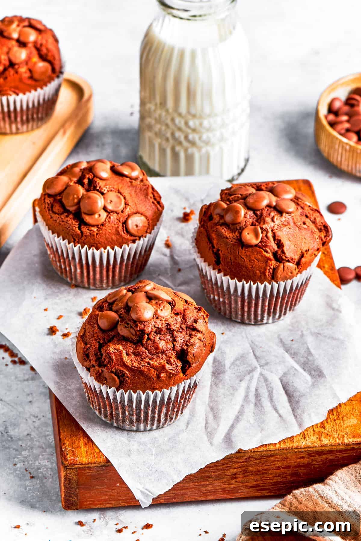 Delicious chocolate muffins presented on a wooden board, ideal for breakfast or a sweet snack. A trio of freshly baked chocolate muffins served on a wooden board, with a glass of milk in the background, creating a cozy scene.