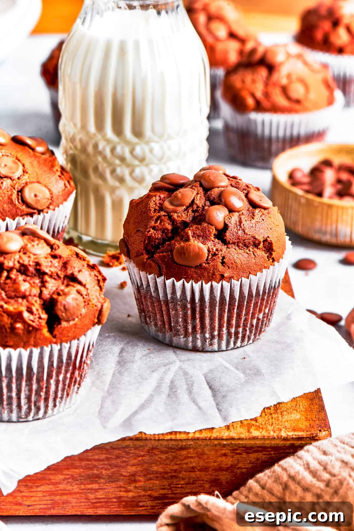 Perfectly baked chocolate muffins presented on a wooden board with a refreshing glass of milk. Freshly baked chocolate muffins served on a rustic wooden board, with a glass of milk in the background.