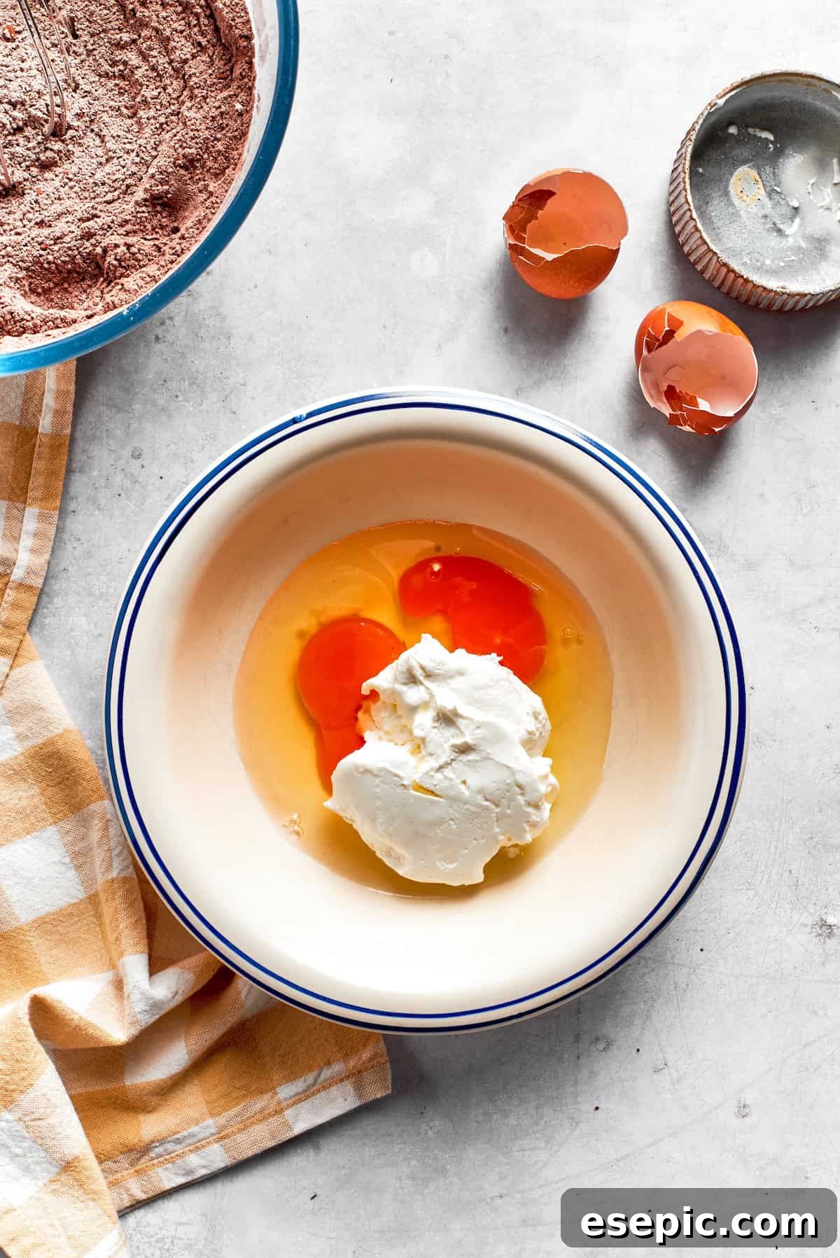 Whisking together eggs and sour cream for the wet mixture. Large eggs are whisked together with creamy sour cream in a separate bowl.