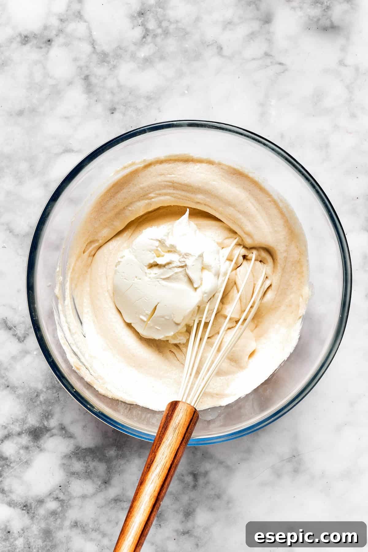 Creamy cheesecake batter is whisked together in a bowl.