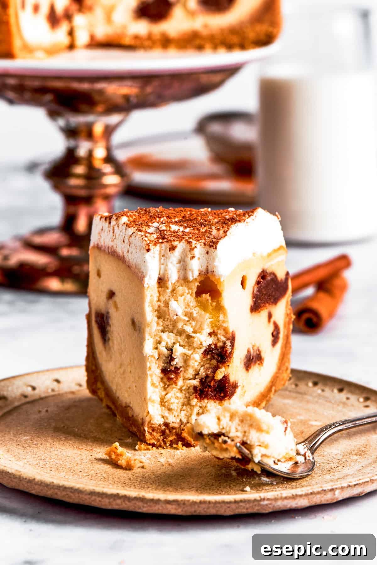 A dessert plate with a slice of cinnamon roll cheesecake with a forkful removed.