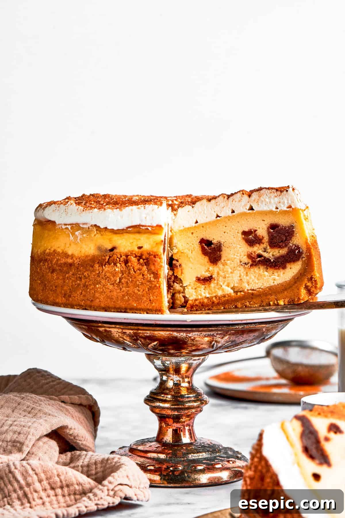 Lifting out a slice of cinnamon roll cheesecake from a whole cheesecake set on a cake platter.