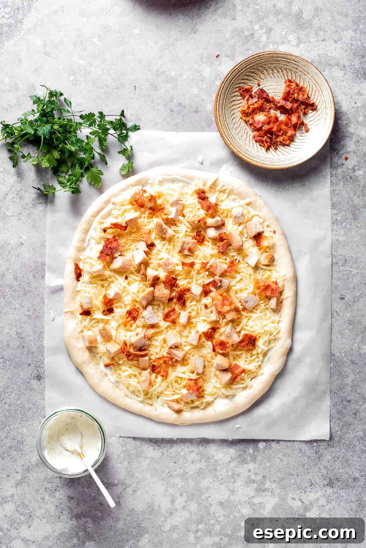 Crispy bacon crumbles are scattered over the chicken and cheese layers on the pizza.