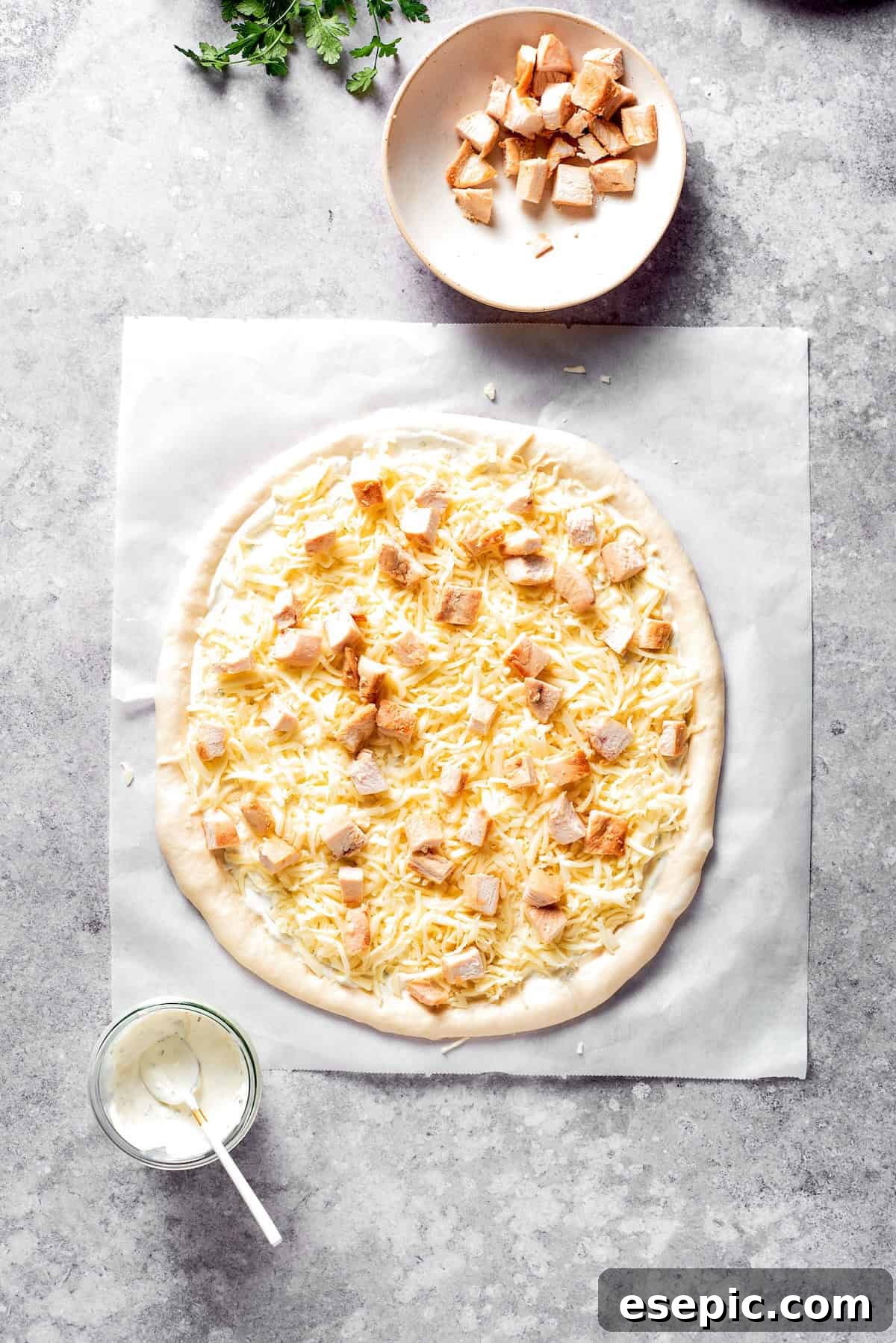 The pizza dough is layered with shredded mozzarella cheese and cooked chicken pieces.