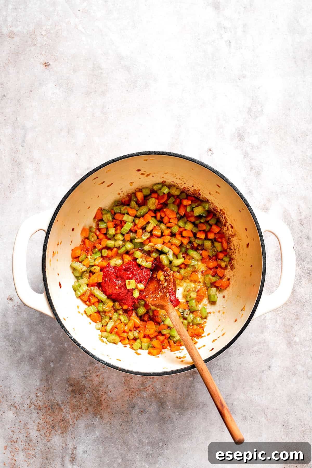 Tomato Florentine soup is deliciously hearty, packed with vegetables, herbs, spinach, and pasta simmered in a tomato-based broth. Tomato paste is stirred into sautéed vegetables in a pot, coating them evenly and enhancing the base flavor.
