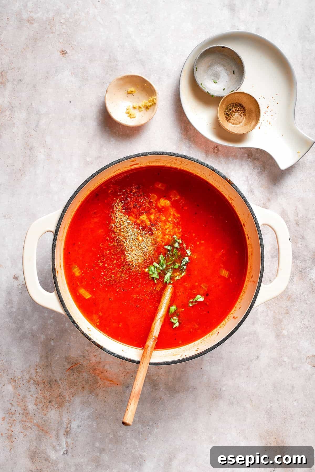 Tomato Florentine soup is deliciously hearty, packed with vegetables, herbs, spinach, and pasta simmered in a tomato-based broth. A mix of Italian herbs and fresh basil being sprinkled into a pot of rich tomato broth.
