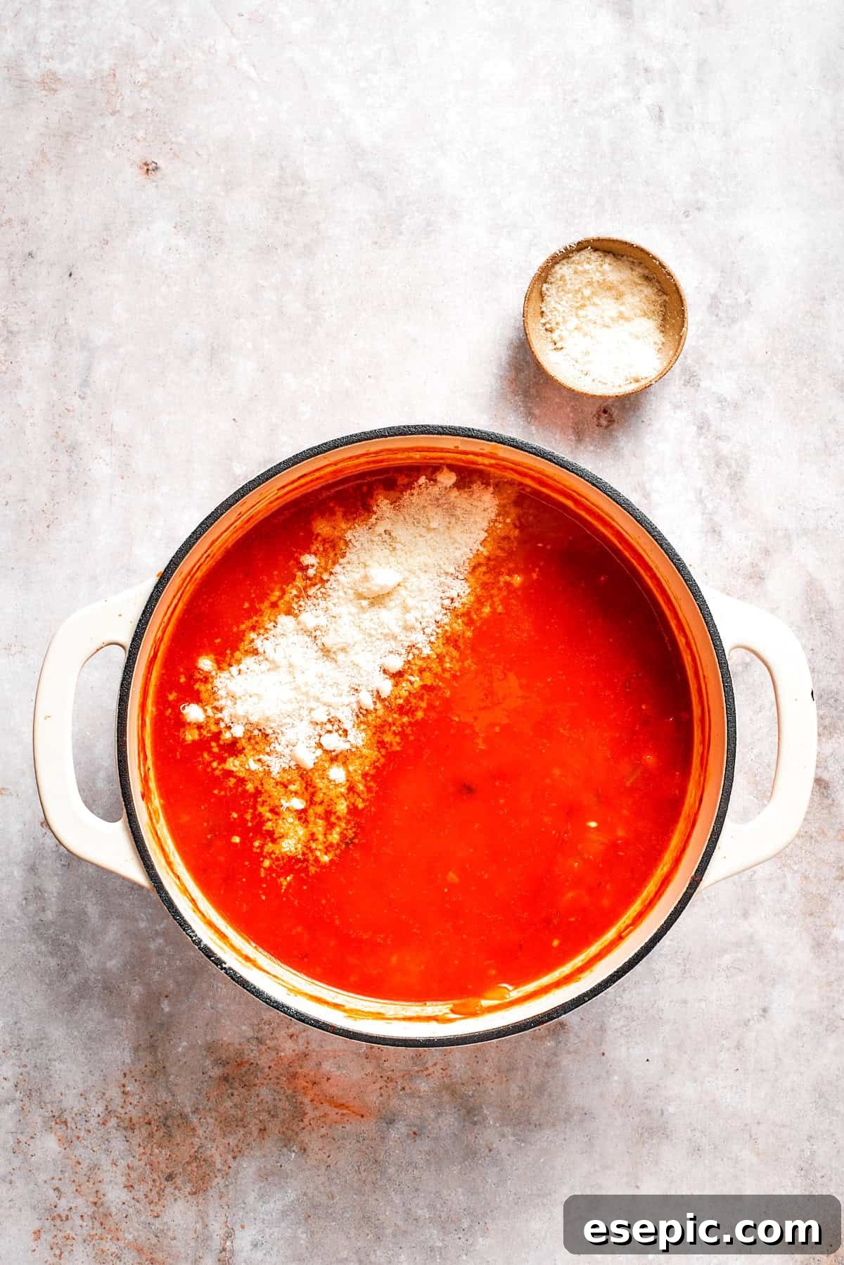 Tomato Florentine soup is deliciously hearty, packed with vegetables, herbs, spinach, and pasta simmered in a tomato-based broth. Grated Parmesan cheese being stirred into a steaming pot of tomato Florentine soup.