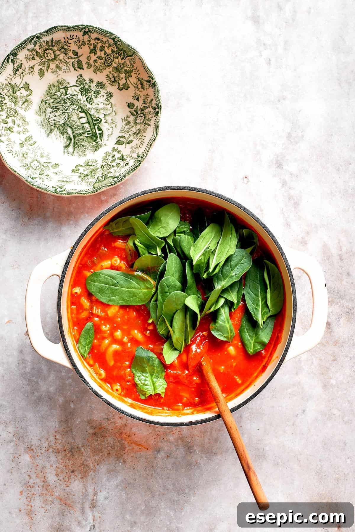 Tomato Florentine soup is deliciously hearty, packed with vegetables, herbs, spinach, and pasta simmered in a tomato-based broth. Fresh spinach leaves being stirred into a pot of vibrant red tomato Florentine soup, wilting beautifully.