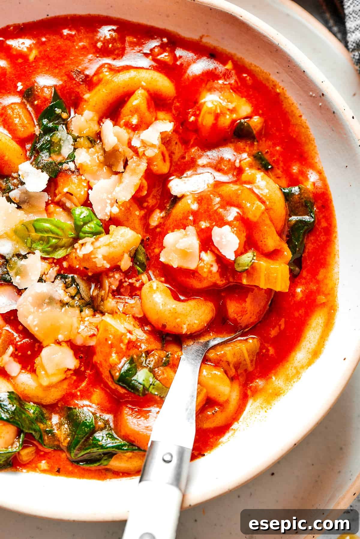 Tomato Florentine soup is deliciously hearty, packed with vegetables, herbs, spinach, and pasta simmered in a tomato-based broth. A spoon stirring through a rich tomato soup, revealing chunks of spinach and small pasta shapes.