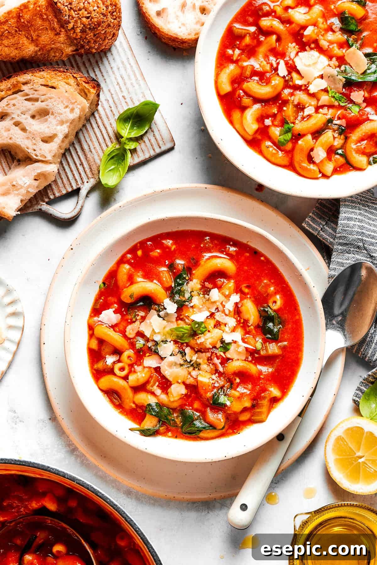 Tomato Florentine soup is deliciously hearty, packed with vegetables, herbs, spinach, and pasta simmered in a tomato-based broth. Two bowls of vibrant tomato Florentine soup, garnished with fresh basil and Parmesan, alongside slices of crusty bread and spoons.
