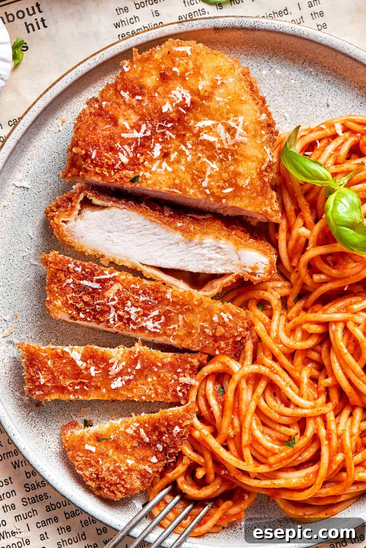 A piece of crusted chicken romano sliced and served with spaghetti.