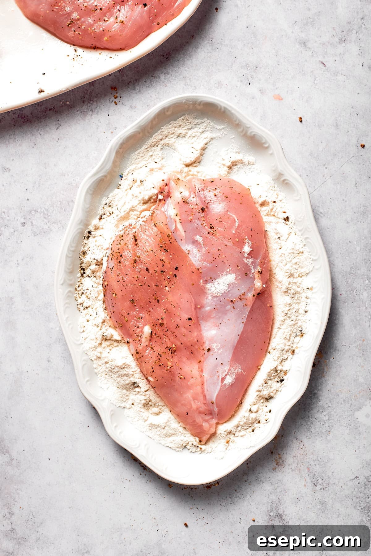 Chicken cutlet being pressed into the seasoned flour mixture.