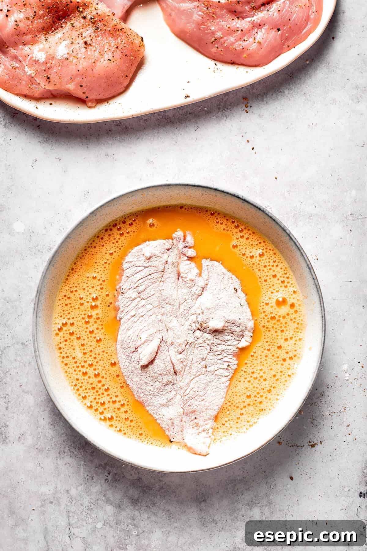 A floured chicken cutlet being dipped into a bowl of whisked eggs.