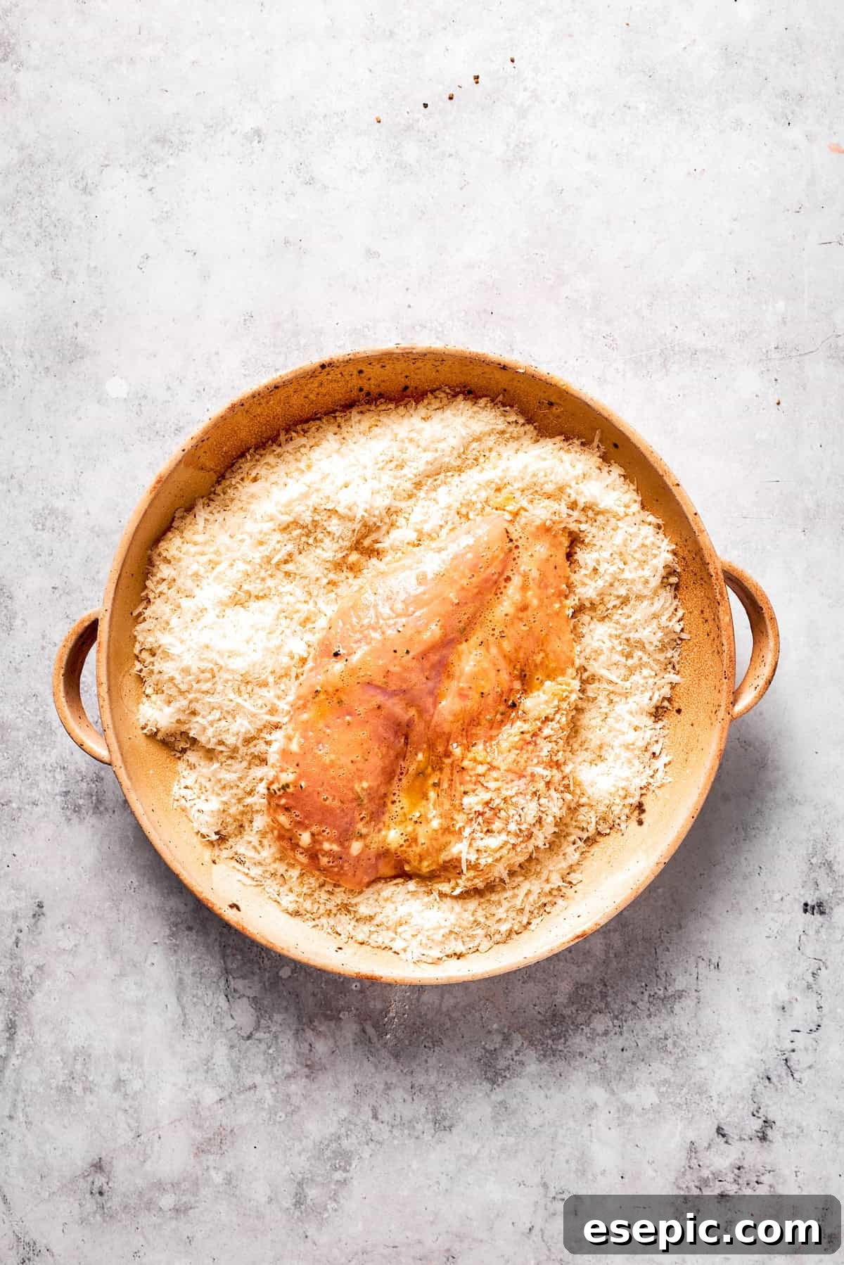 An egg-coated chicken cutlet being pressed into the breadcrumb and cheese mixture.