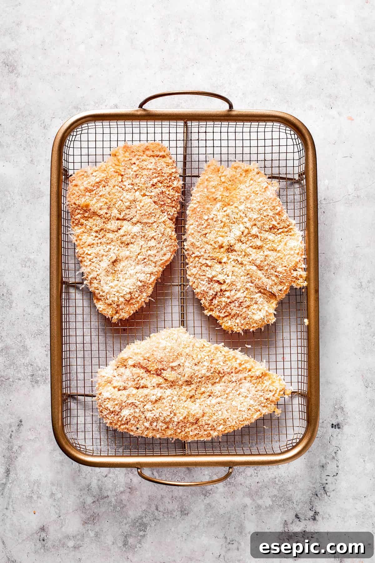 Three perfectly breaded chicken cutlets arranged on a plate, ready for frying.
