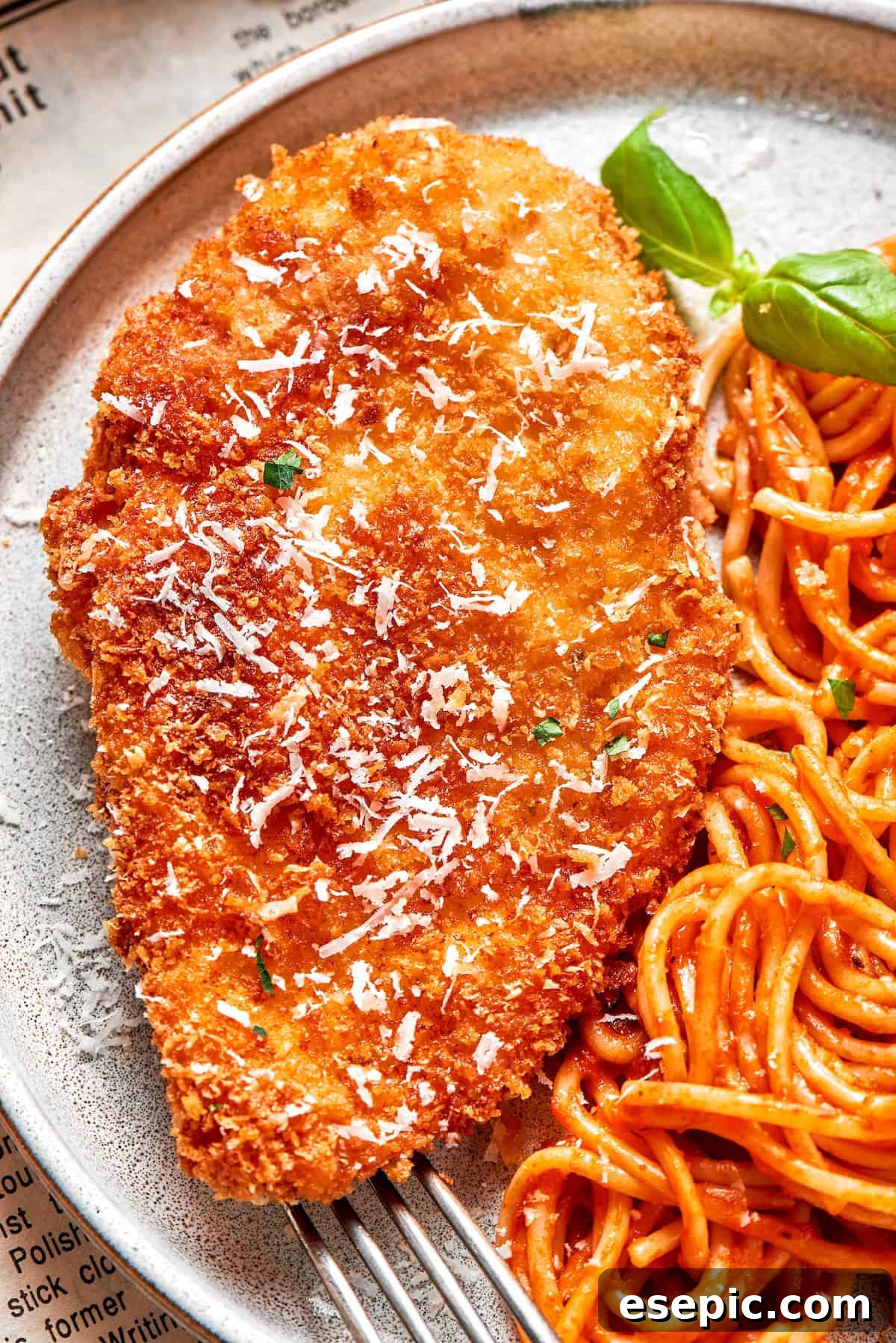 A big piece of crusted chicken romano served with spaghetti.