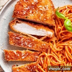 A piece of crusted chicken romano sliced and served with spaghetti.