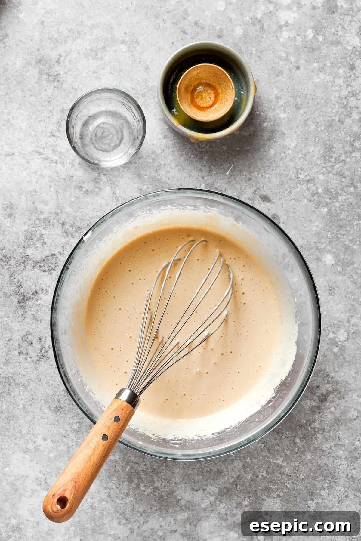 A whisk blending the wet ingredients for the carrot cake, such as eggs, sugar, and oil.