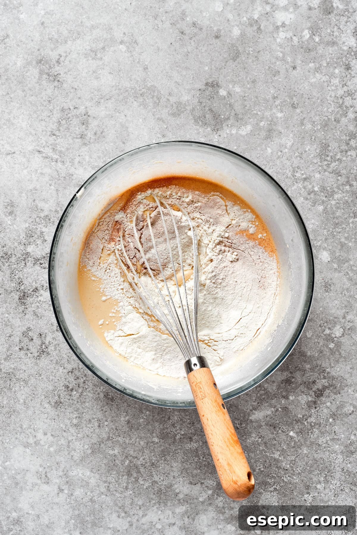 Dry carrot cake mix being gently added to the wet mixture, ensuring proper blending.