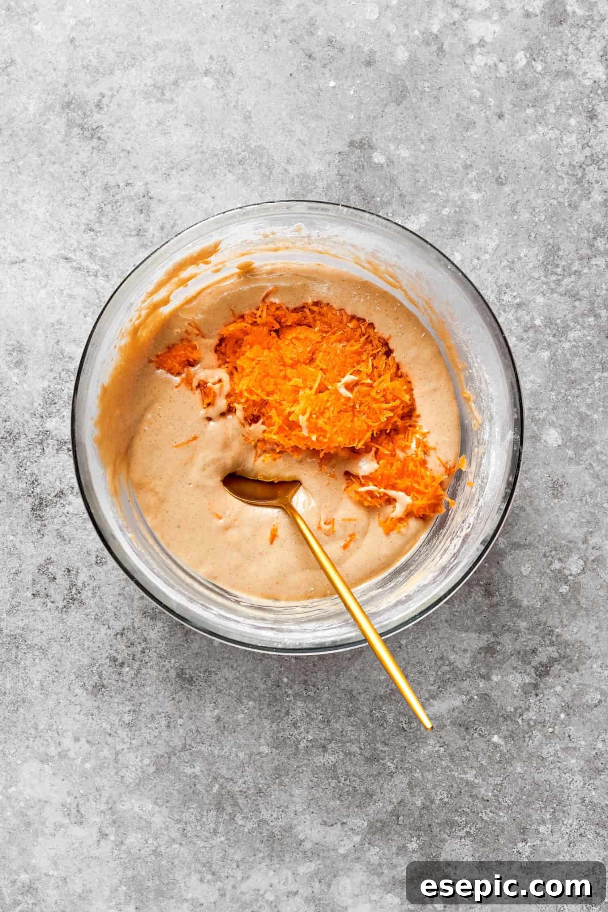 Finely grated carrots being folded into the carrot cake batter, adding natural sweetness and moisture.