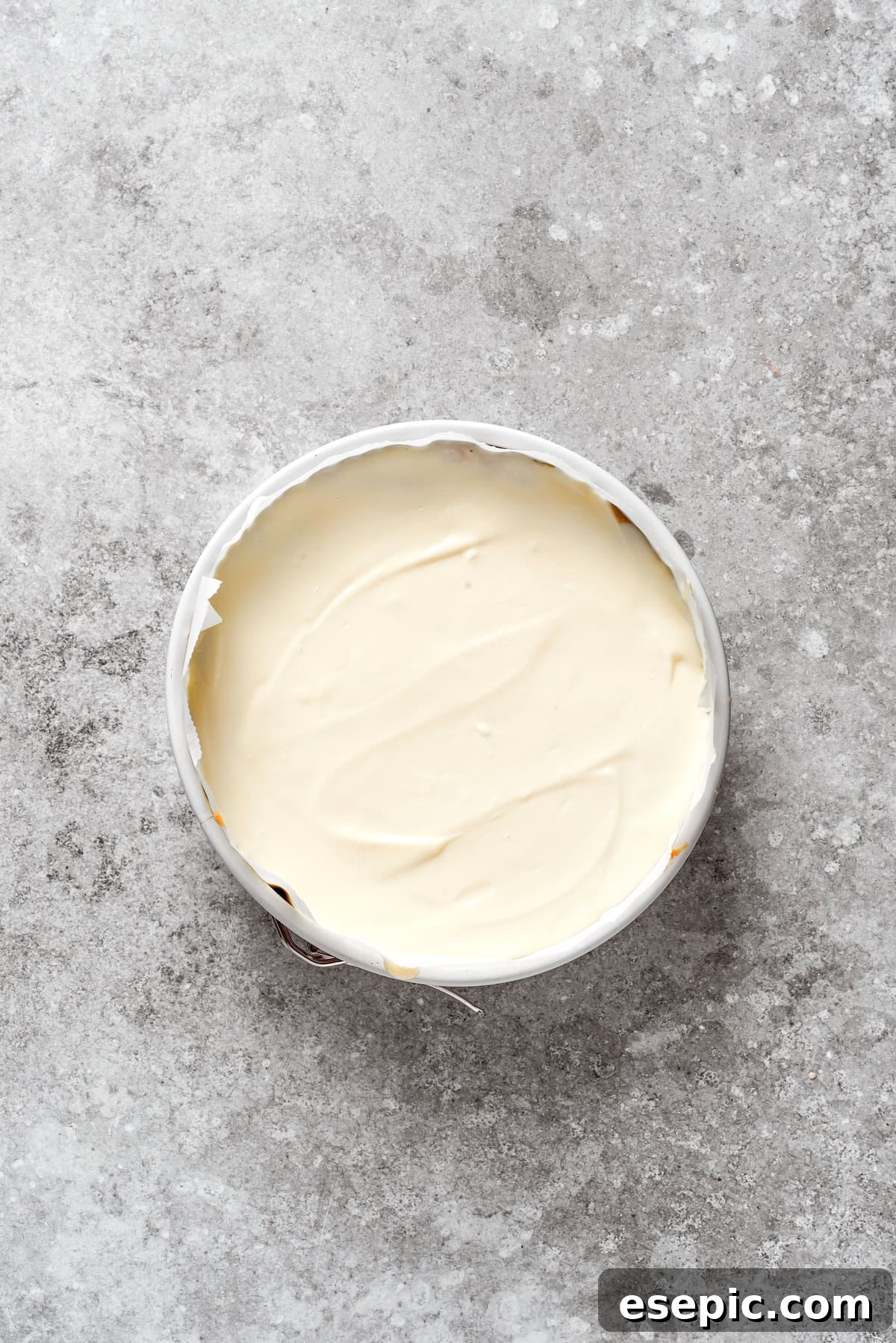 Cheesecake batter being poured over the carrot cake layer, creating distinct layers.