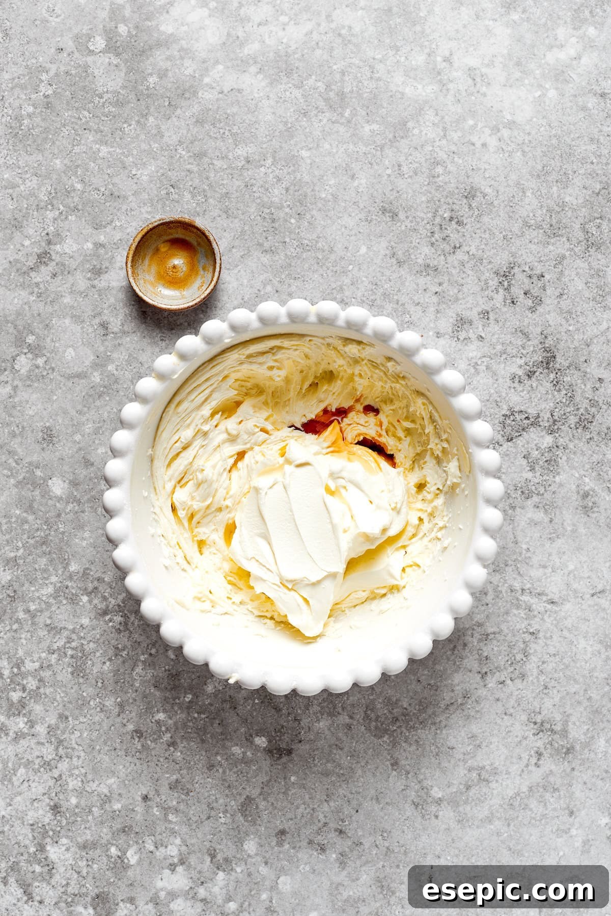 Vanilla extract being added to a bowl of freshly made cream cheese frosting, indicating the final touch for flavor.
