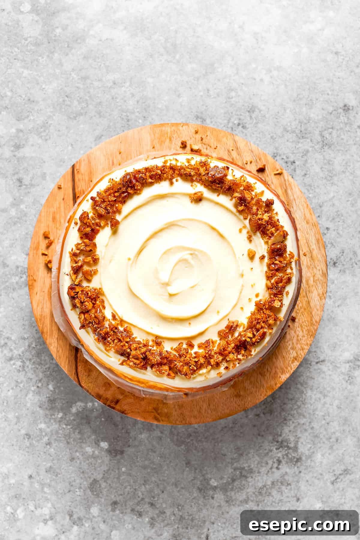 A fully assembled carrot cake cheesecake, adorned with cream cheese frosting and caramelized pecans, on a wooden cake stand.