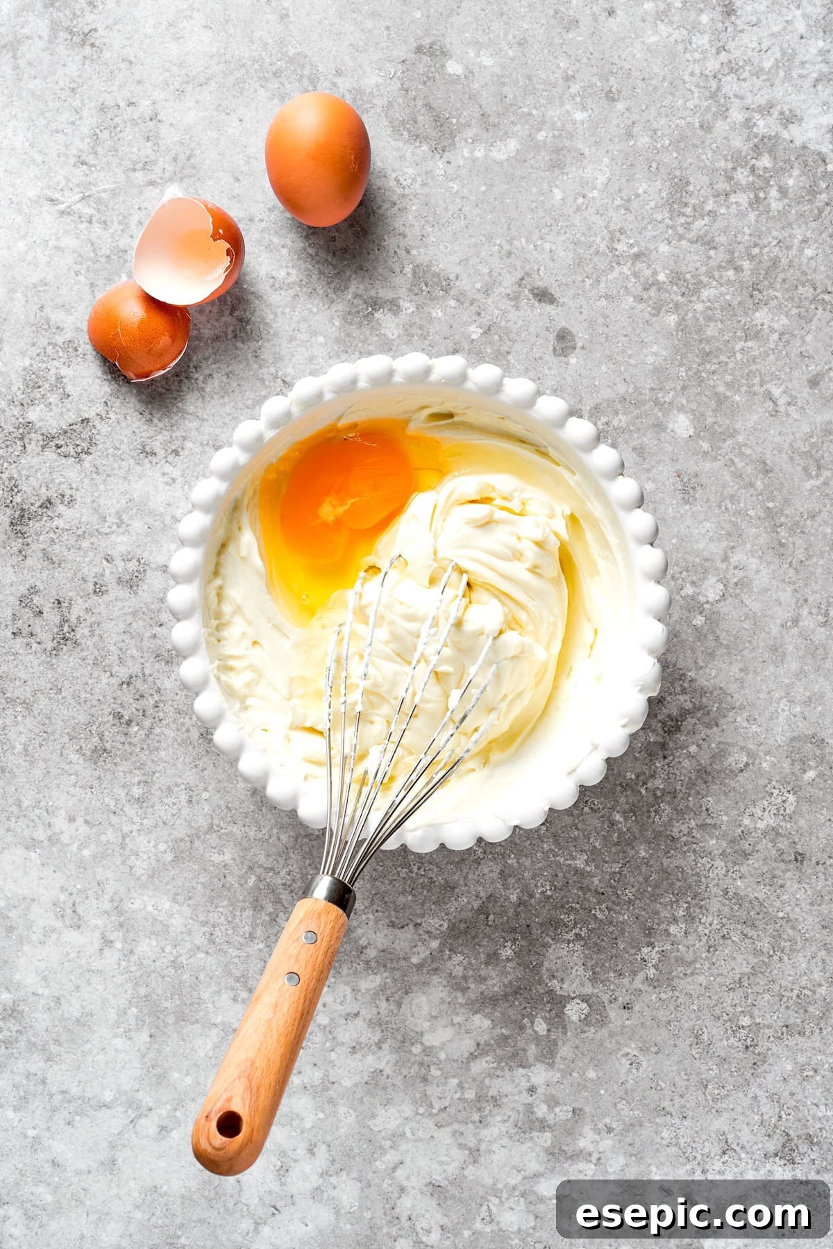 Eggs and cream cheese being whisked together in a bowl, illustrating the initial steps of the cheesecake batter preparation.