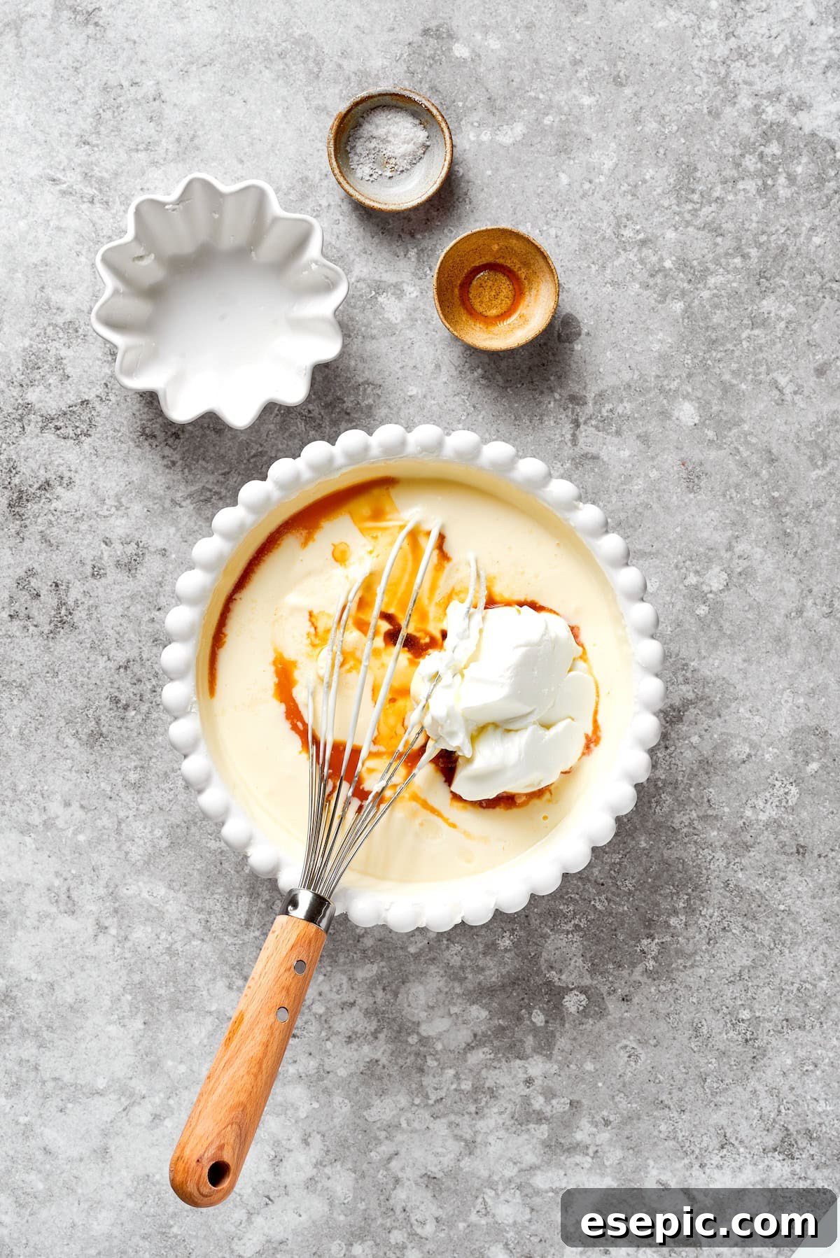 Vanilla extract being poured into the cheesecake batter, signifying the addition of flavor enhancers.
