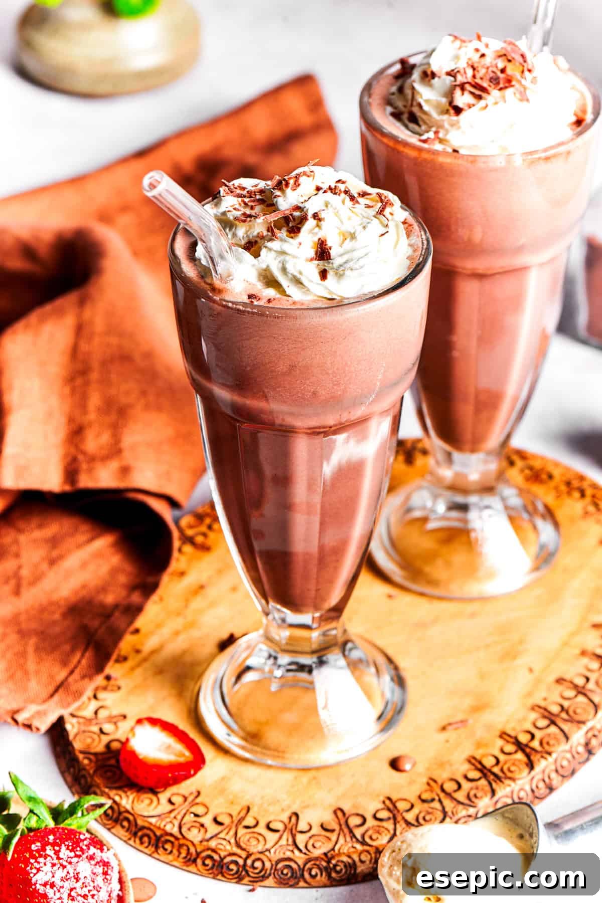 Two exquisitely prepared chocolate milkshakes, adorned with whipped cream and chocolate shavings, are presented side-by-side on a elegant wooden tray, ready to be enjoyed.