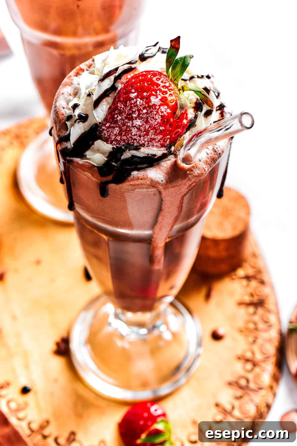 A perfectly blended chocolate milkshake, generously topped with whipped cream, a scattering of fresh strawberries, and an artistic chocolate drizzle, served in a tall glass.