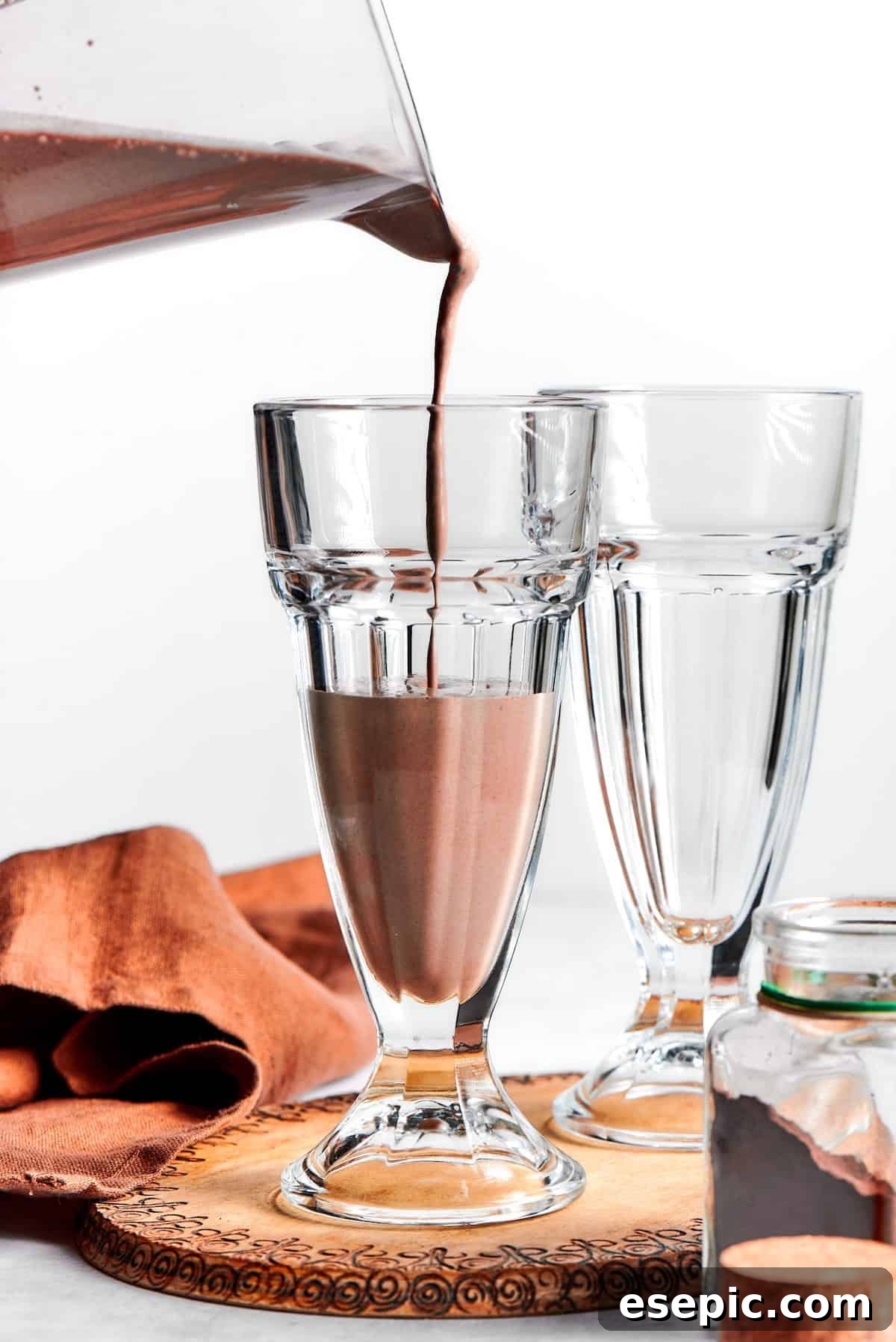 A stream of thick, rich chocolate milkshake is being poured from a blender into a tall, chilled glass, ready for enjoyment.