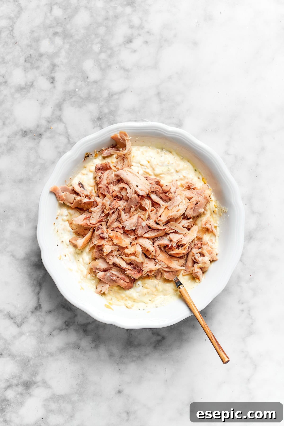 Shredded chicken being stirred into the creamy, cheesy casserole base.