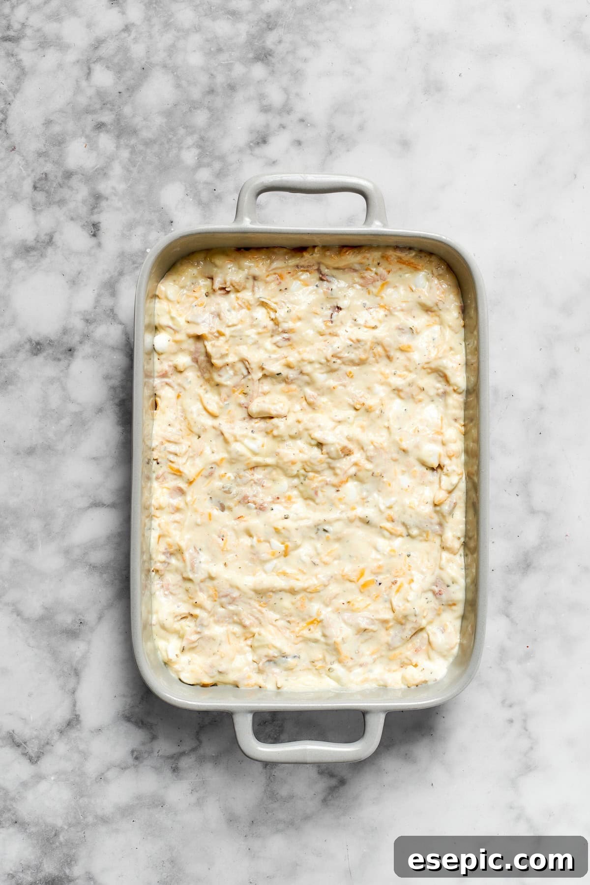 The assembled chicken casserole mixture being transferred into a baking pan.