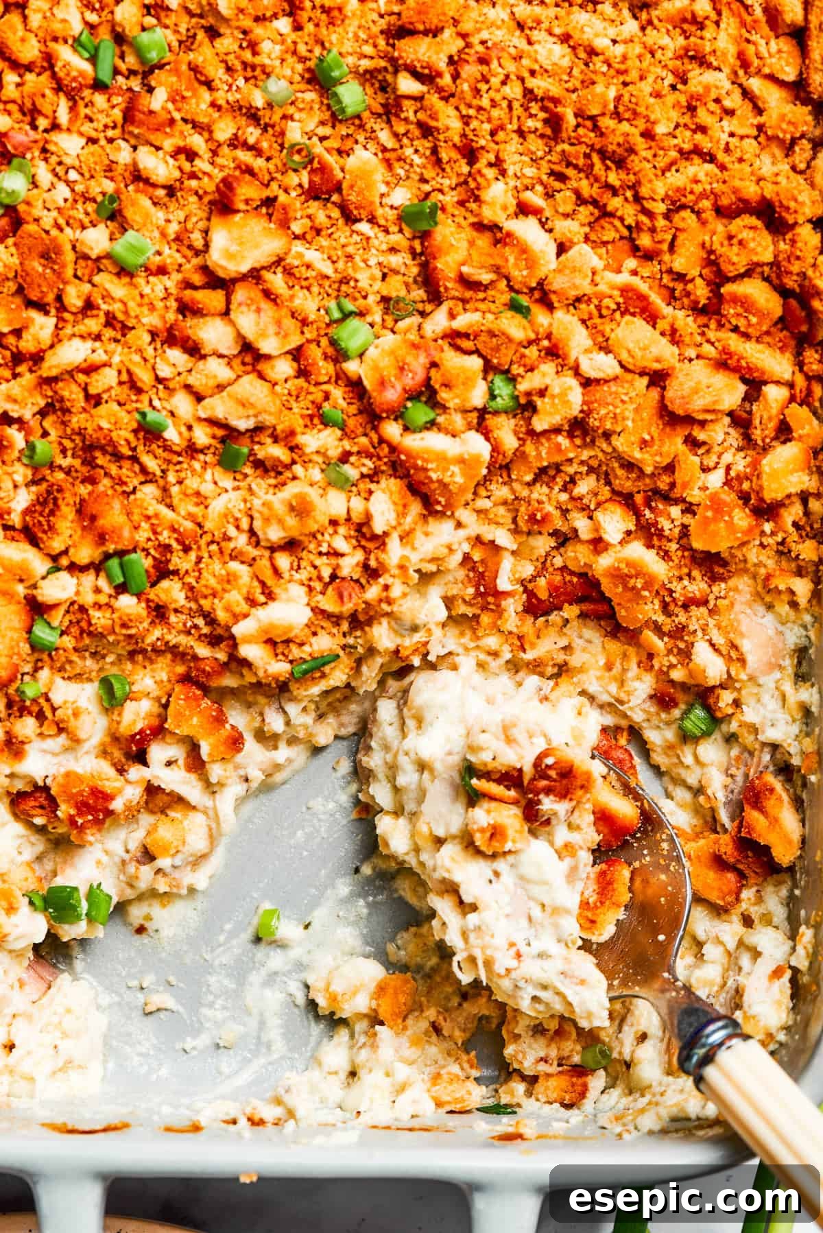 A serving spoon digging into the creamy, cheesy Million Dollar Chicken Casserole, showing its delightful texture.