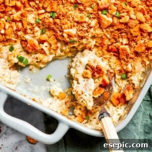 A serving spoon scooping out million dollar chicken casserole from a baking dish.
