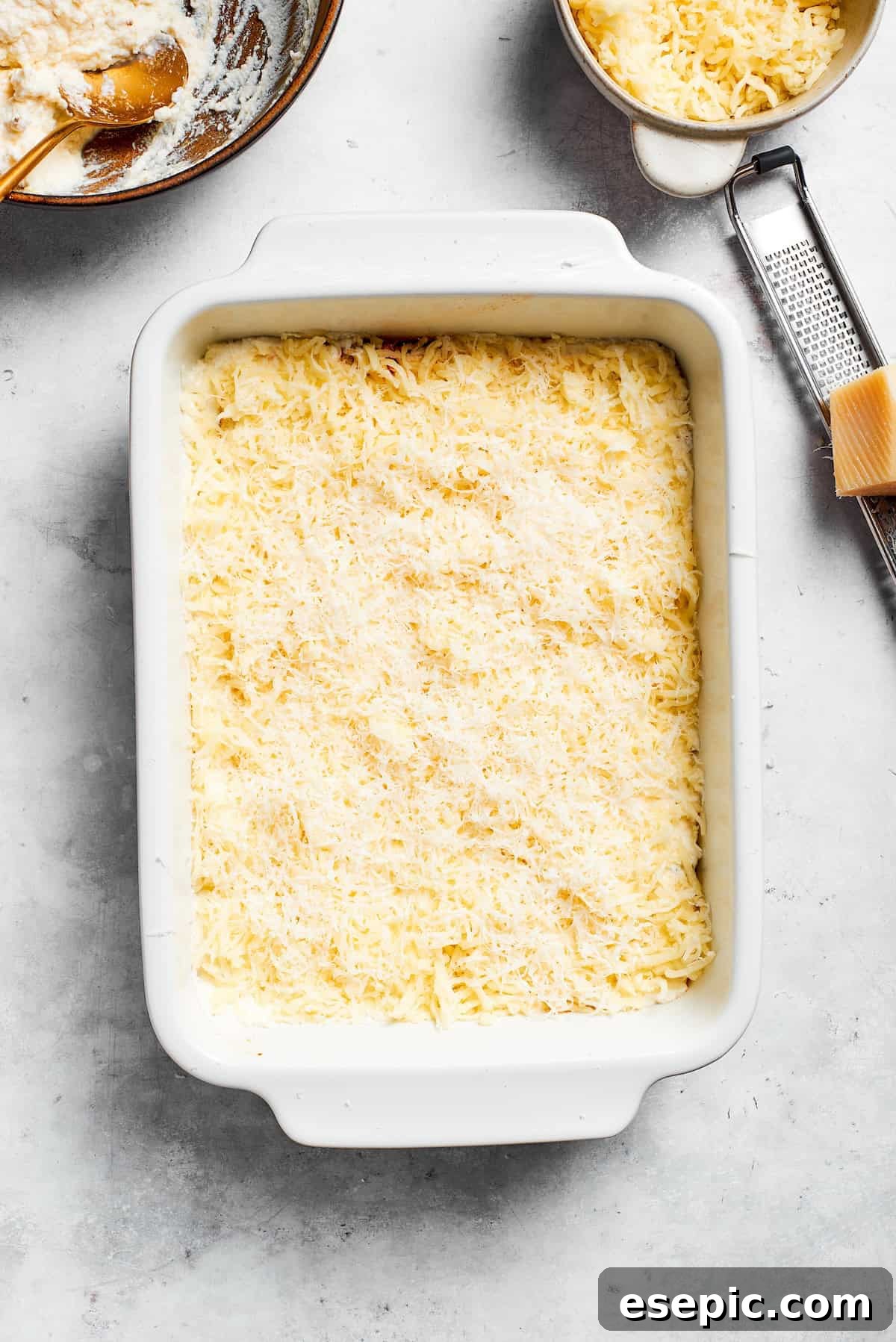 The best beef lasagna recipe is packed with tons of meaty, cheesy flavor and a rich and savory sauce. Make ahead friendly! Shredded mozzarella and Parmesan cheese being sprinkled over the ricotta layer in a lasagna dish.
