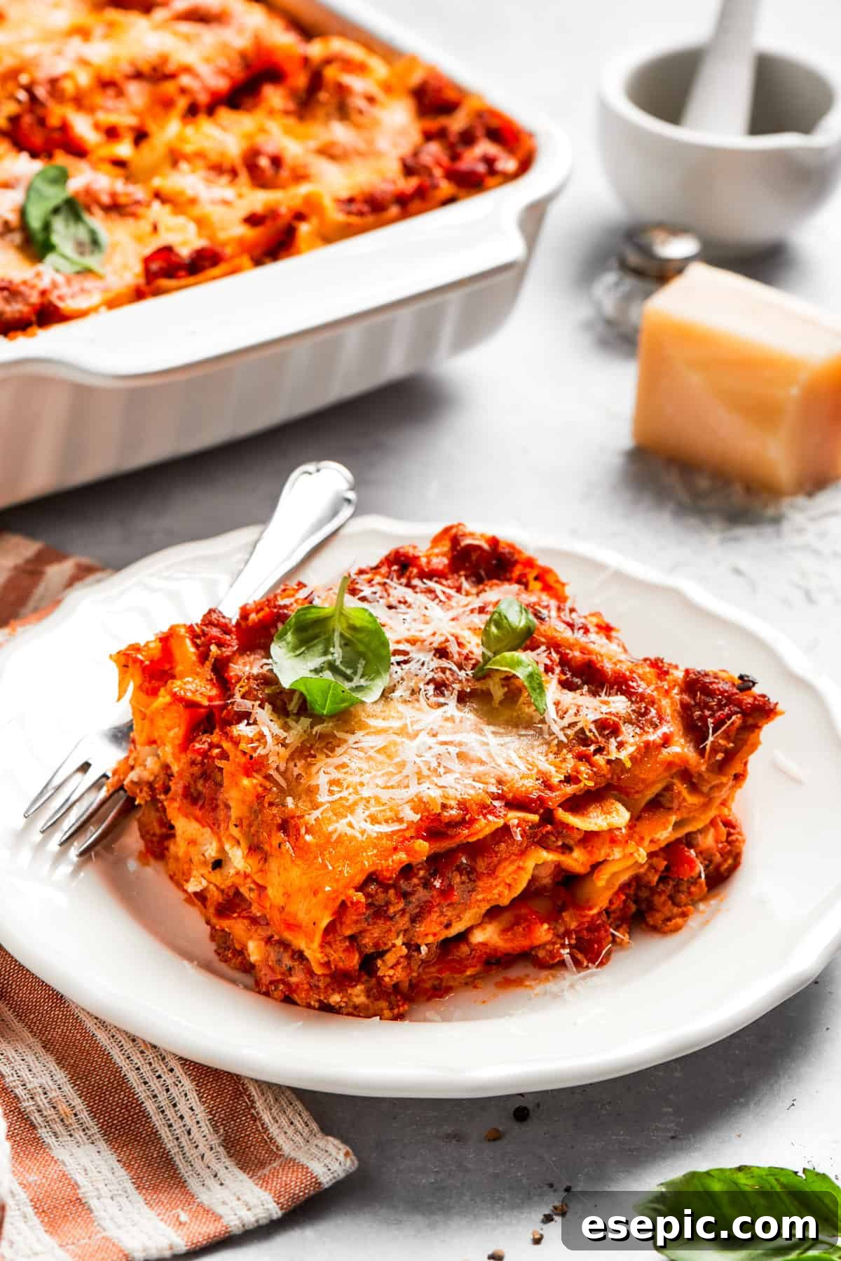The best beef lasagna recipe is packed with tons of meaty, cheesy flavor and a rich and savory sauce. Make ahead friendly! A generous serving of homemade beef lasagna served on a dinner plate with a fork, ready to be enjoyed.