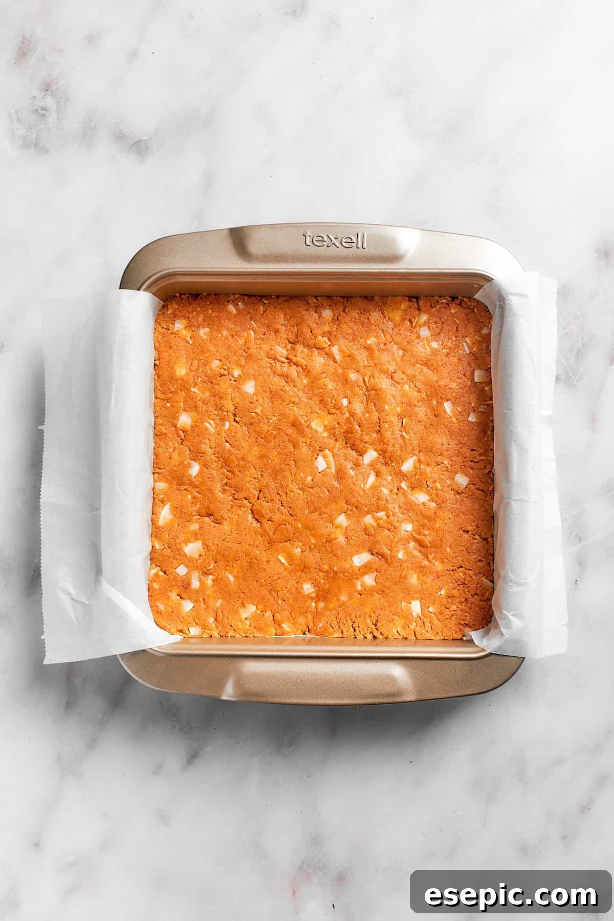 The graham cracker crust base firmly pressed into a parchment-lined 8x8-inch baking pan, ready for chilling.