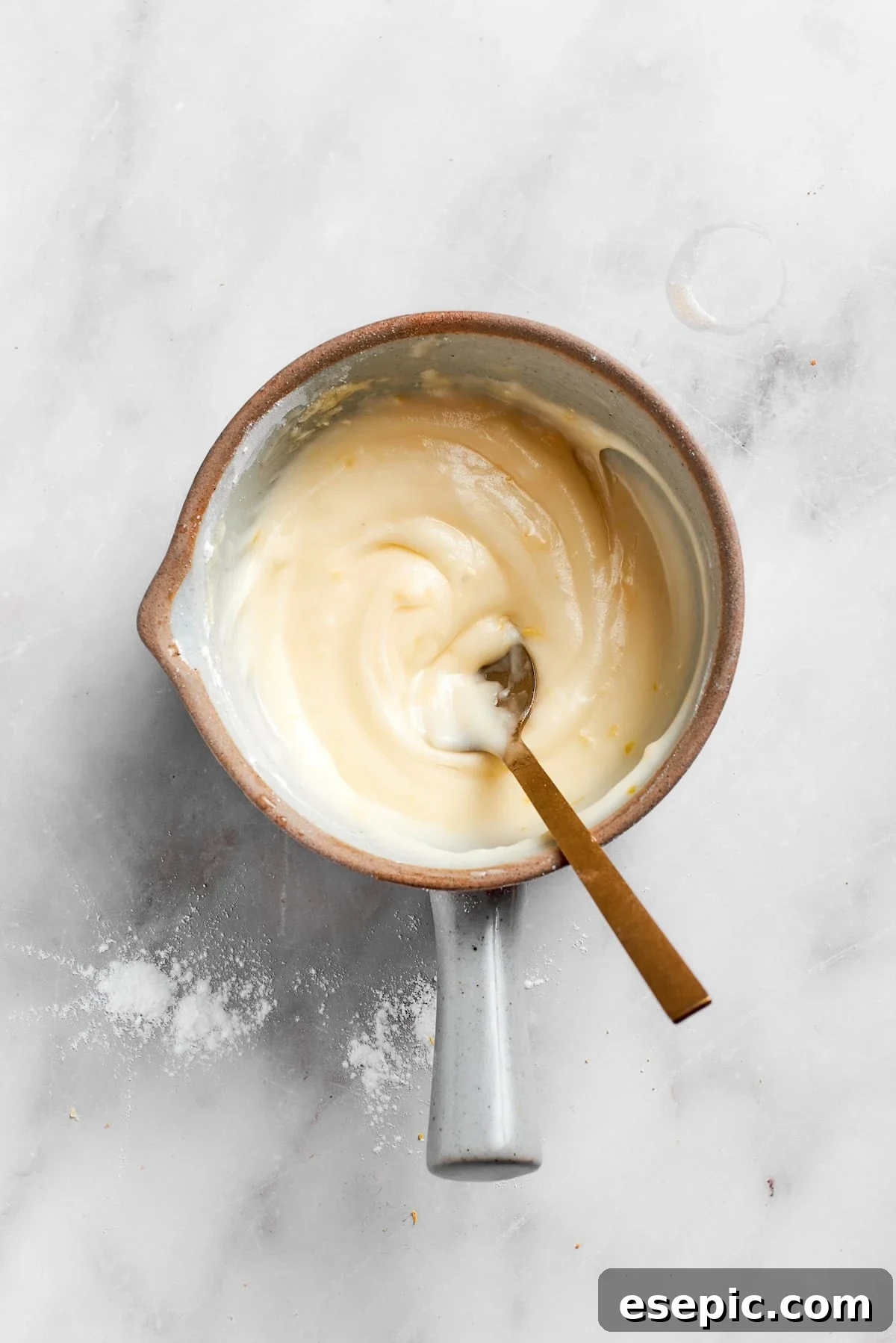 A spoon stirring the ingredients for the lemon slice frosting, which appears thick and creamy in the bowl.