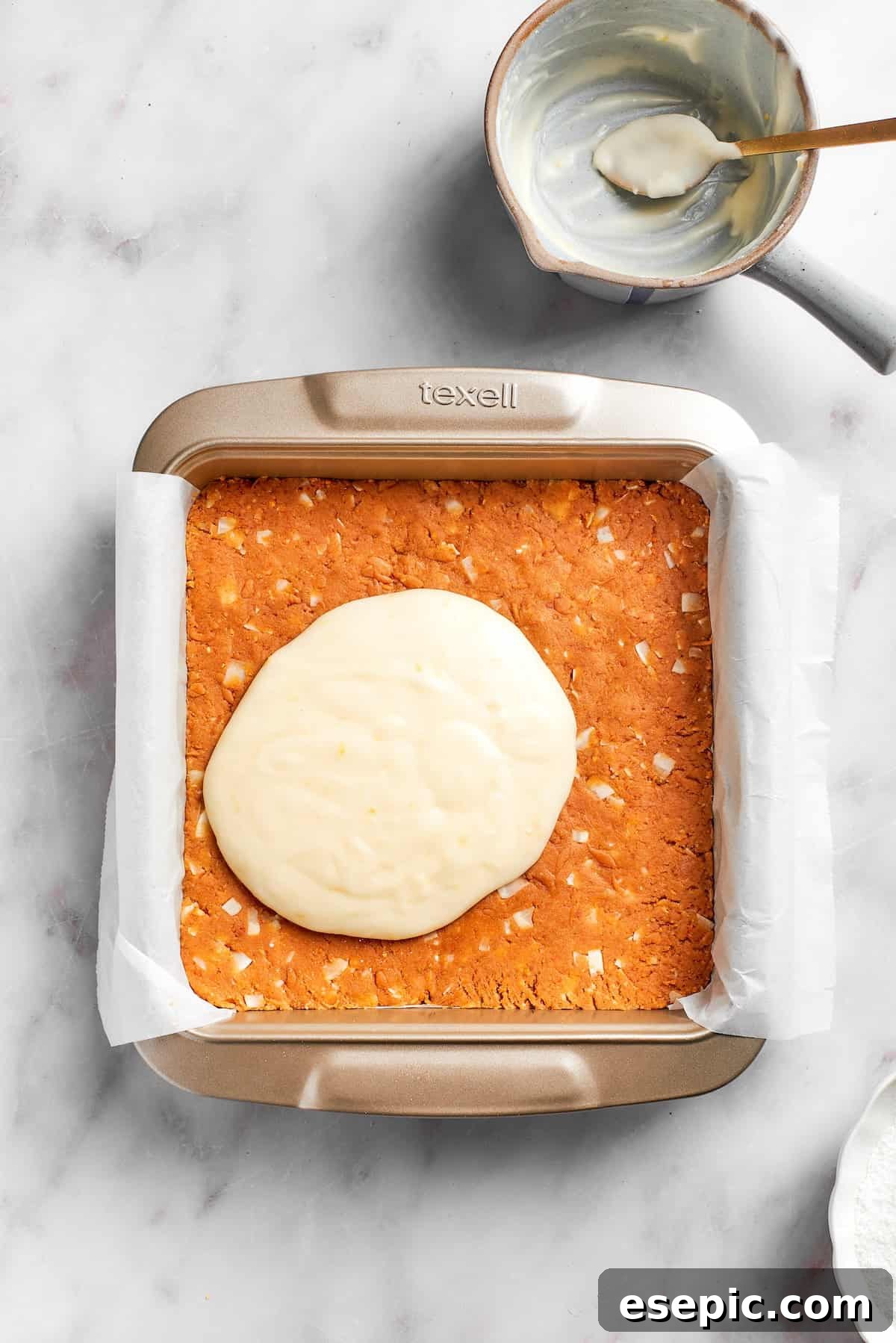 The creamy lemon frosting being spread evenly over the chilled graham cracker crust in a baking pan.