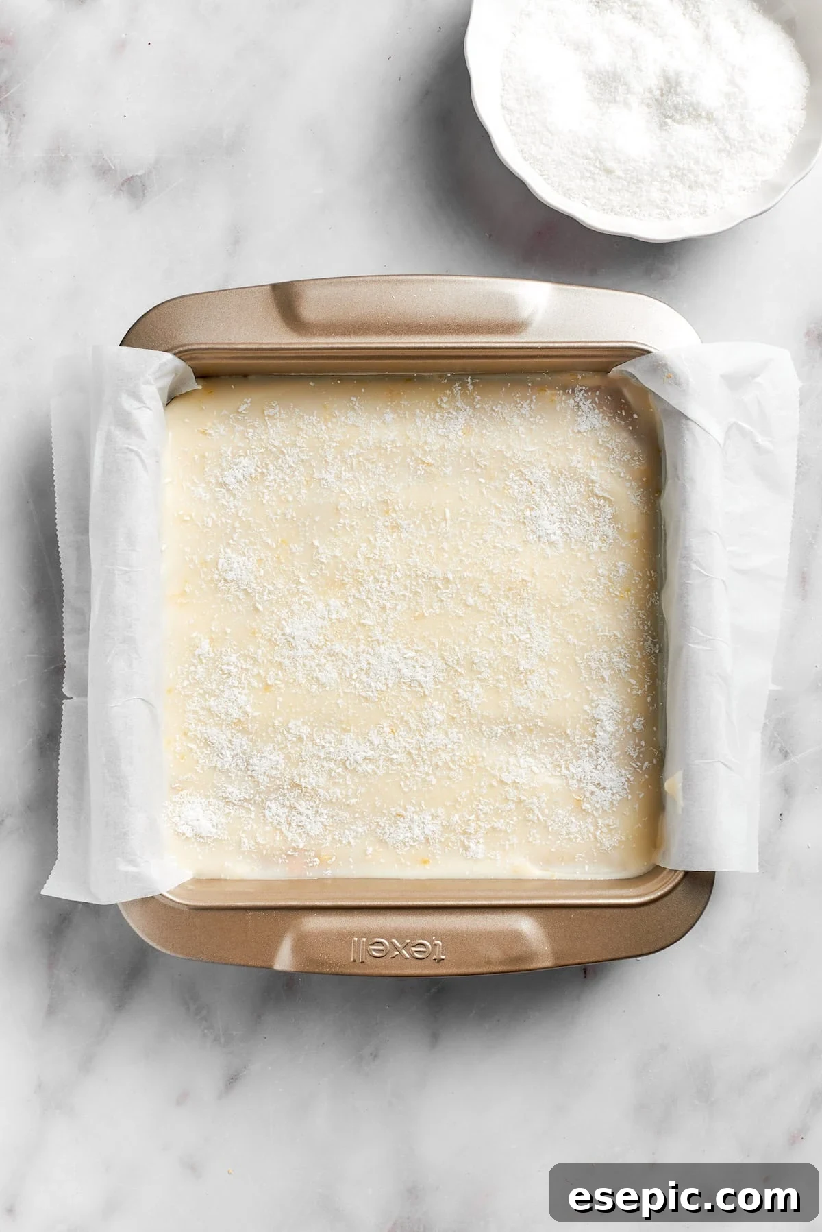 The completed lemon slice in a parchment-lined pan, topped with frosting and sprinkled coconut, ready for its final chill.