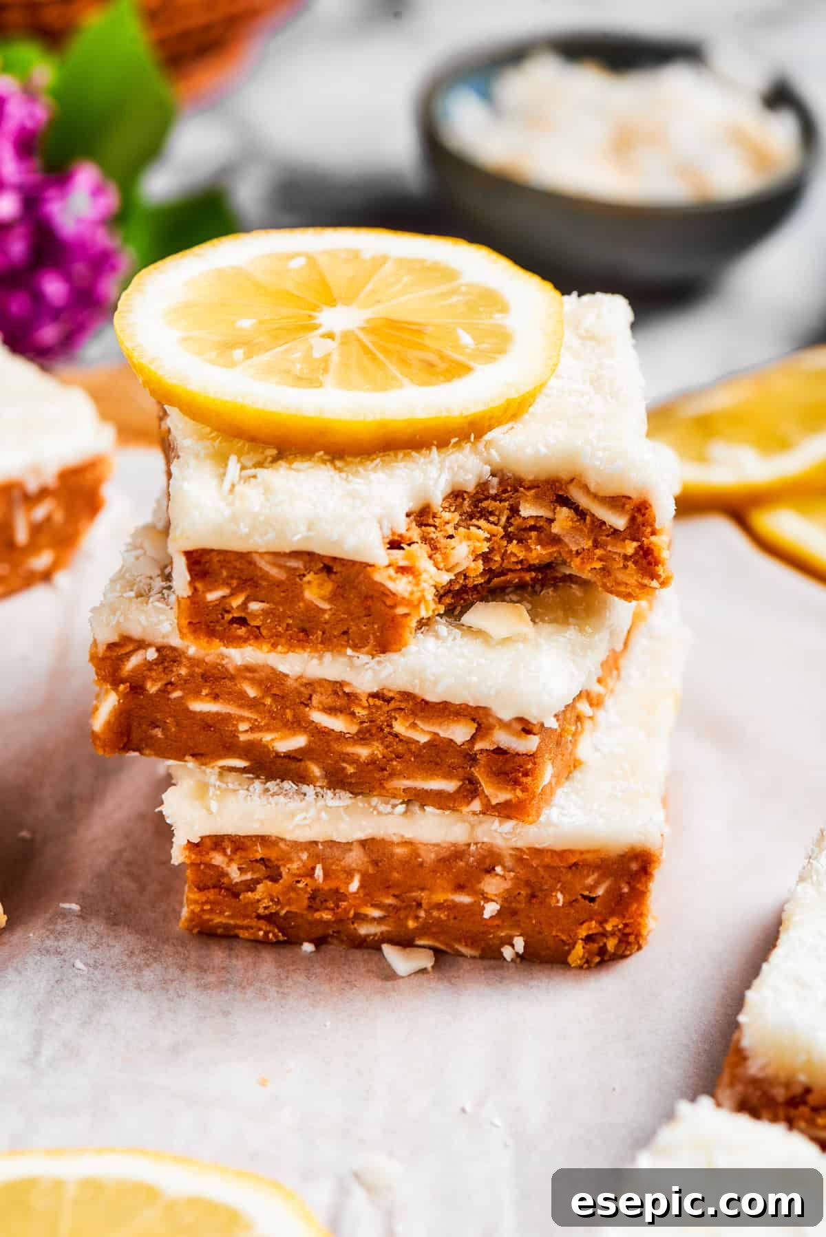 Three lemon slice squares stacked with a bite missing from the top one, revealing the dense base and creamy frosting.