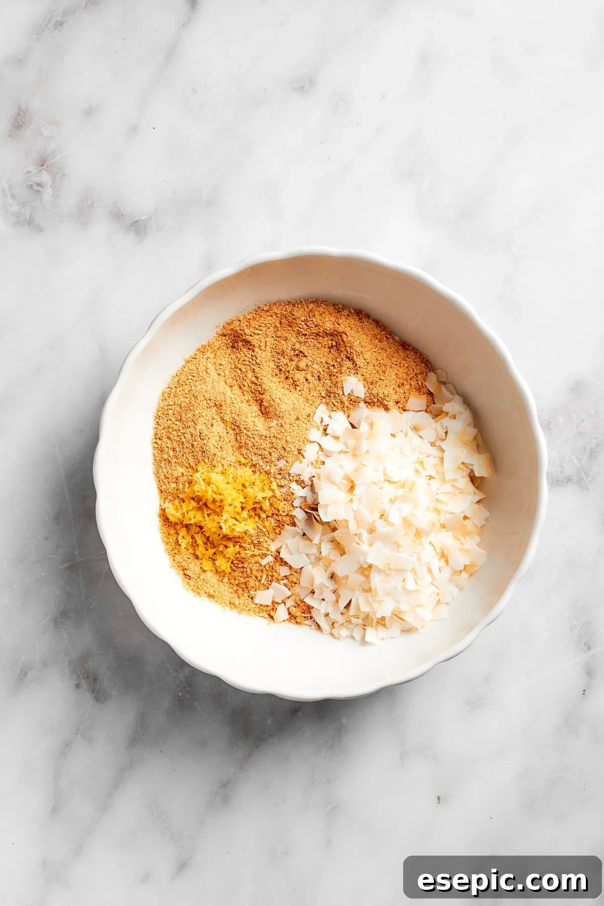 Sweetened flaked coconut being added to finely crushed graham crackers in a large mixing bowl, ready for combining.