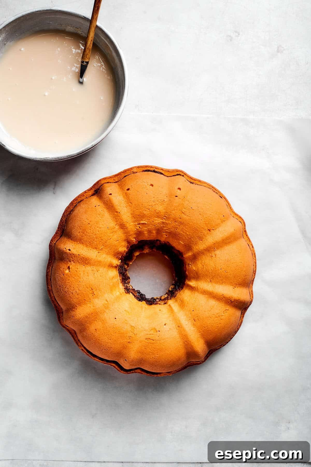 An easy recipe for Sock It To Me Cake, a tender coffee cake with a ribbon of brown sugar, cinnamon and toasted pecans through the center. A bowl of icing next to a cooled cake.