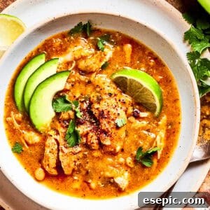 A close-up of a rustic bowl filled with steaming spicy chicken soup, garnished with avocado and lime, highlighting its hearty texture.