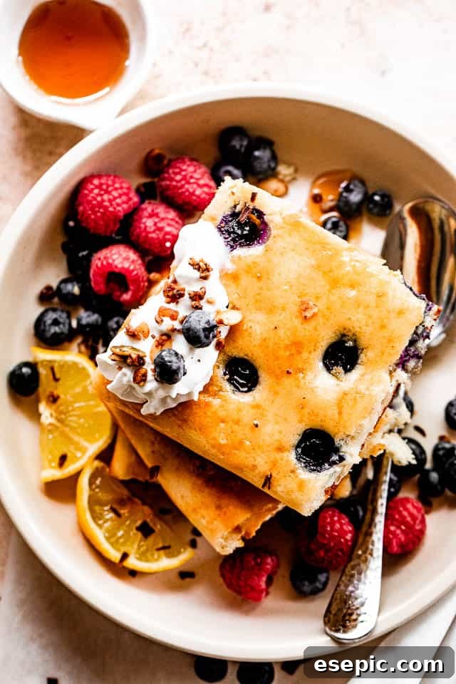 top shot of squared pancakes topped with whipped cream, berries around the pancakes, and maple syrup to the side