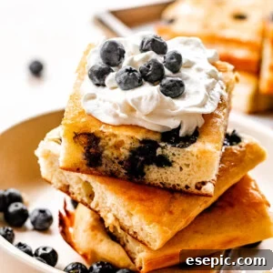 side shot of stacked sheet pan pancakes topped with whipped cream and blueberries