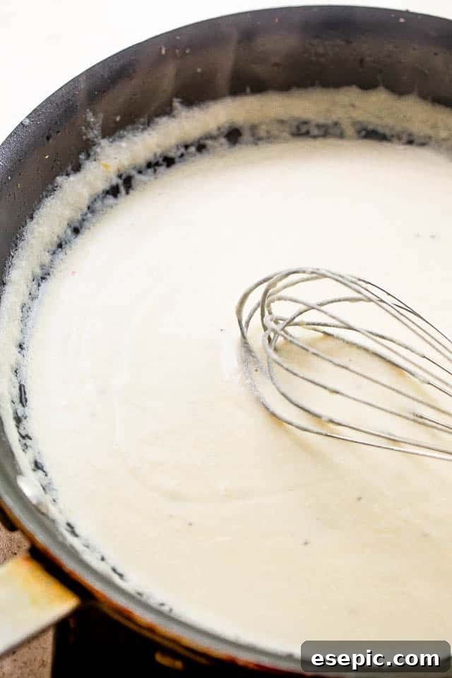 Whisking cream cheese sauce in a black skillet, showing the creamy texture forming